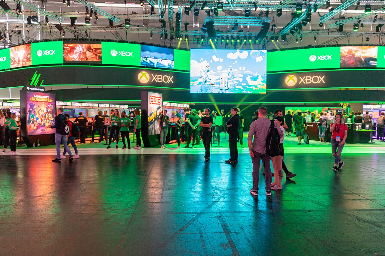 Visitors at the Xbox stand at Gamescom in 2019, below green Xbox signs.